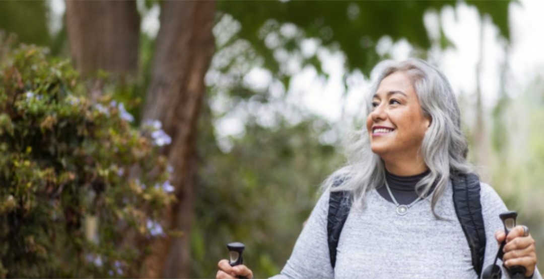 Mid shot portrait of a woman with grey hair smiling and hiking in nature